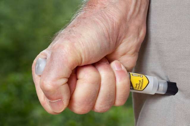 Hand pressing Epipen into outer thigh through clothing