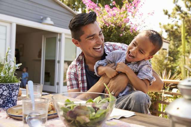 Father holding laughing young son at outdoor dining table