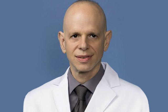 A headshot of Dr. John Belperio who is wearing a white lab coat and a dark tie