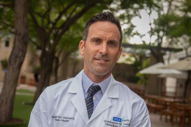 Dr Christopher Tarnay in white lab coat and tie, outdoor portrait