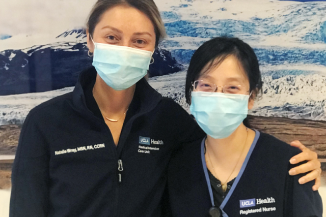 two nurses in a hospital wearing masks, looking at the camera and embracing
