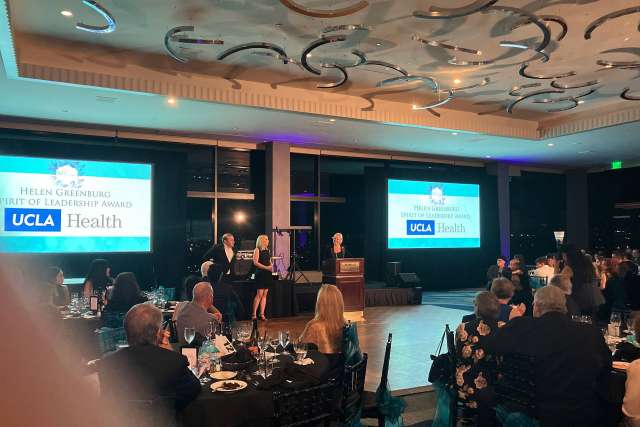 Dinner event with attendees facing stage and UCLA Health logo on screens