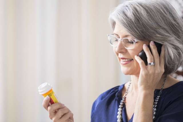 Woman with gray hair holding prescription bottle while on phone