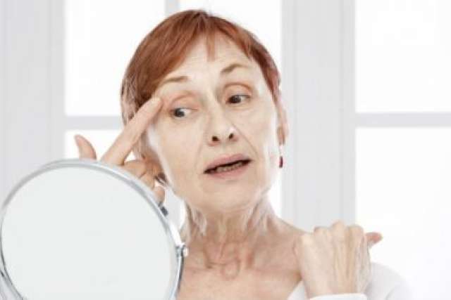Woman with wrinkles checking face in small round mirror.