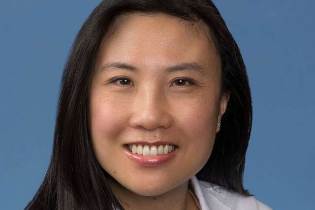 Kara Chew smiling in a white coat against a blue background.