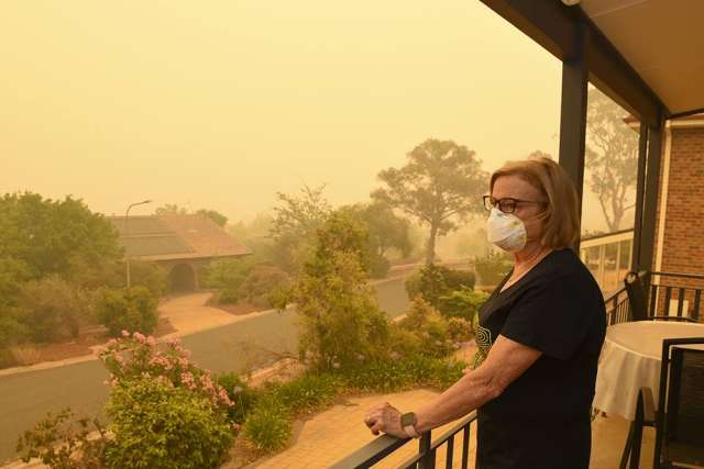 Masked person on porch overlooking smoky orange neighborhood