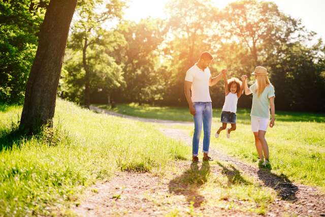 Two adults and two children on sunlit park path surrounded by trees