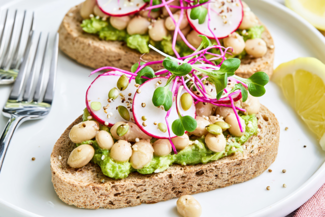 Whole grain toast with mashed avocado, radish slices, white beans, and microgreens.