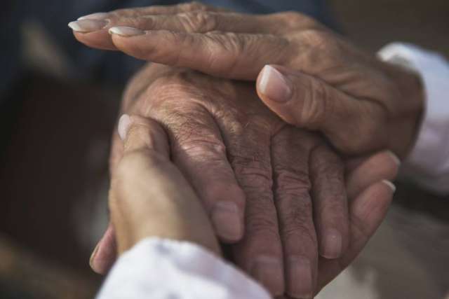 Close-up of two hands gently holding an elderly hand, symbolizing care, support, and compassion.