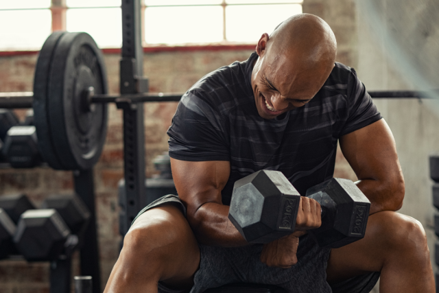 A man sitting on a gym bench lifting weights to increase his biceps muscle