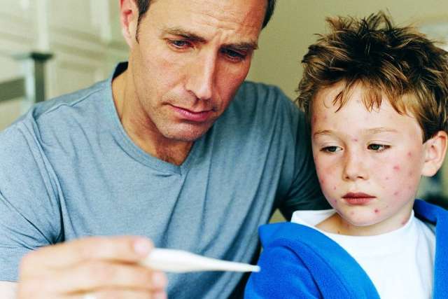 Man checking thermometer while boy with red spots