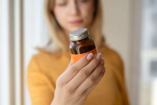 Person holding small amber medicine bottle with white cap