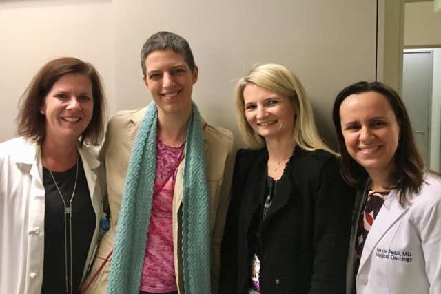 Four women, including Lori Jordan (center with short hair, tan blazer, and teal scarf), stand together smiling in a professional setting.