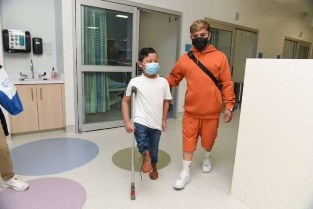 Efrain Ordoñez Jr using a crutch to walk through hospital alongside Jose Luis Hernandez