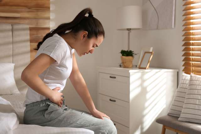 Young woman suffering from stomach ache on bed at home, space for text.
