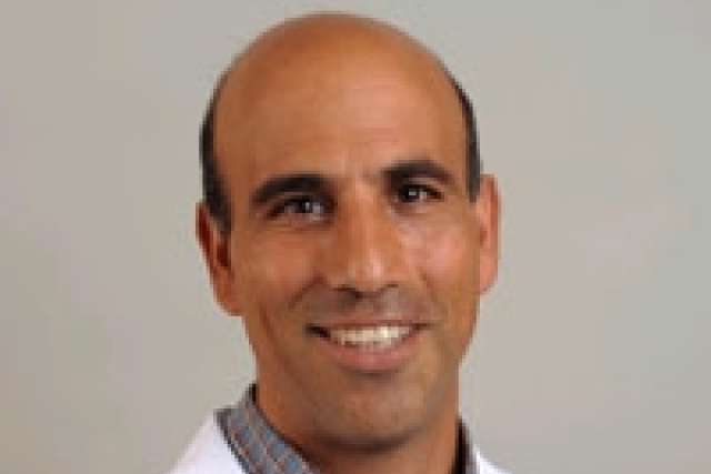  A headshot of Dr. Robert Ashley, a bald man with dark eyes and a warm smile, wearing a collared shirt under a white lab coat.