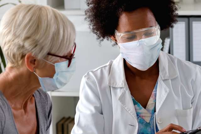 A doctor with a face shield and mask discussing with a masked patient.