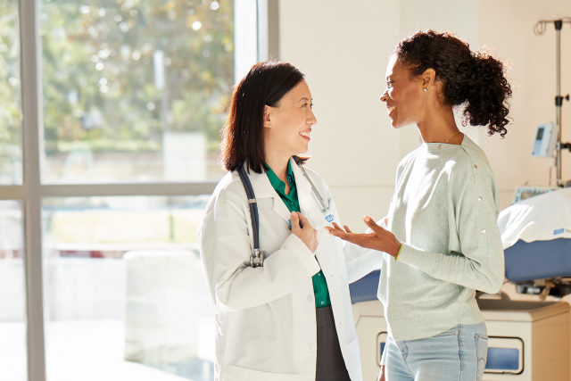 Two women converse in a medical office with natural light coming through windows.