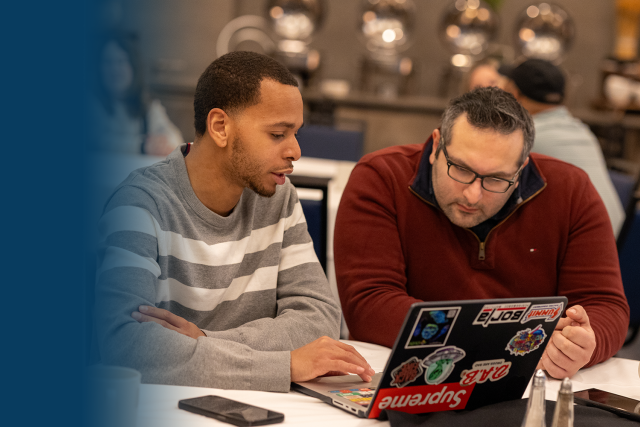 Two people collaborating at a table with a laptop and an open book