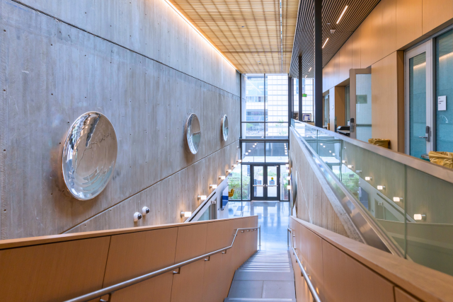 Modern interior hallway at UCLA’s CASIT building featuring wood and glass finishes, wall-mounted art, and natural light from floor-to-ceiling windows.