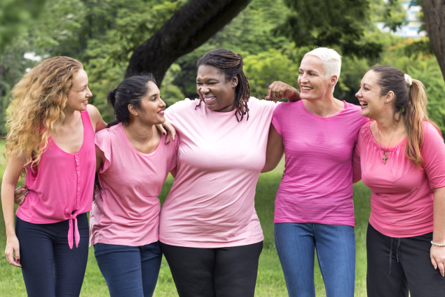 Group of 5 breast cancer survivors wearing pink shirts, with their arms around each other, smiling