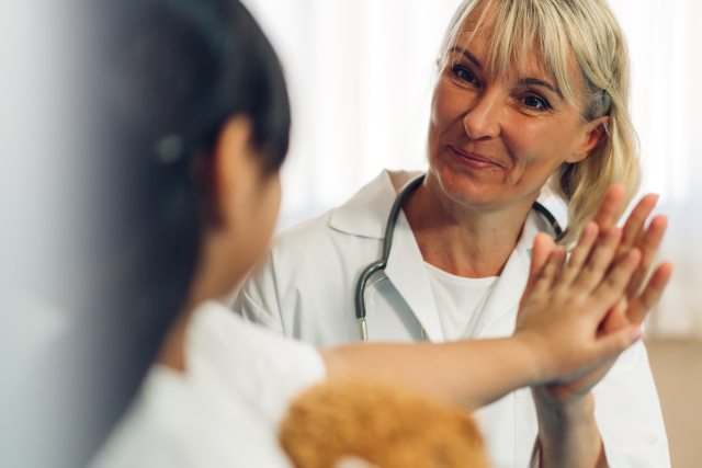 Woman doctor wearing protective mask talking to little girl patient