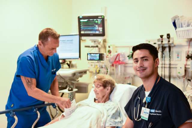 Two nurses sitting on either side of a patient laying on a hospital bed.