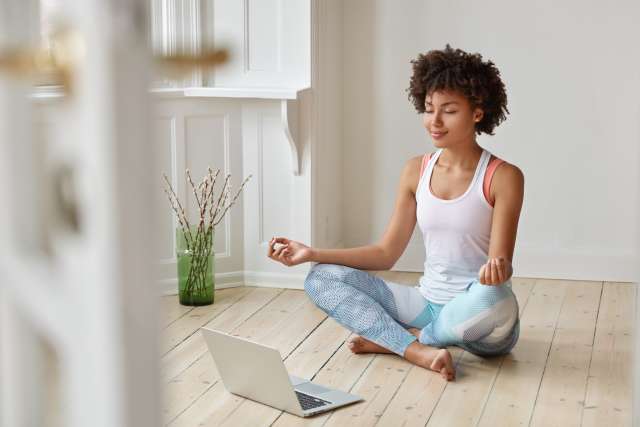 Woman meditating indoors with assistance of laptop