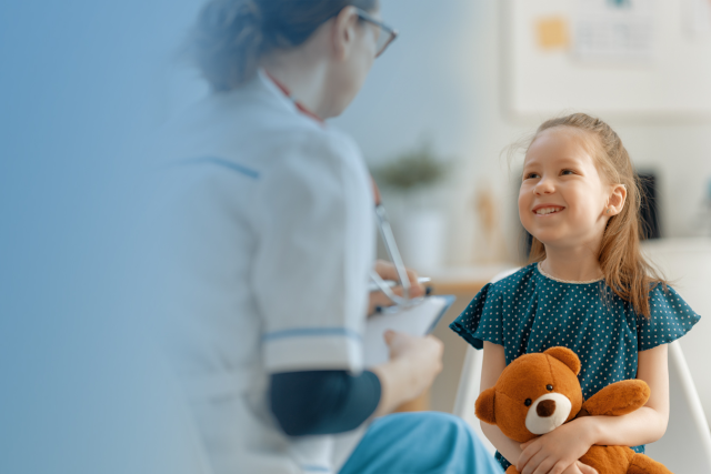 A women physician talking to a little girl holding a brown teddy bear.