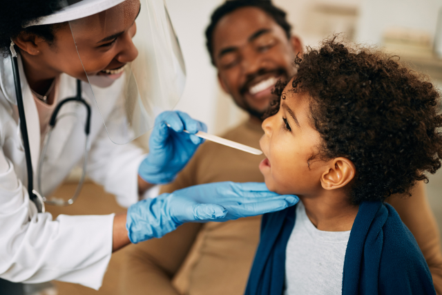Pediatrician looking into child's mouth with tongue depressor