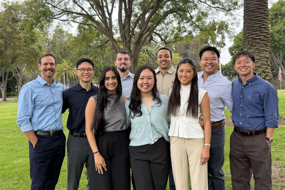 Ten smiling adults standing outdoors near a palm tree