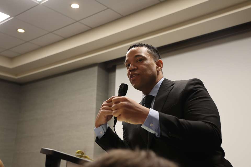 Man in suit speaking at podium, holding a microphone