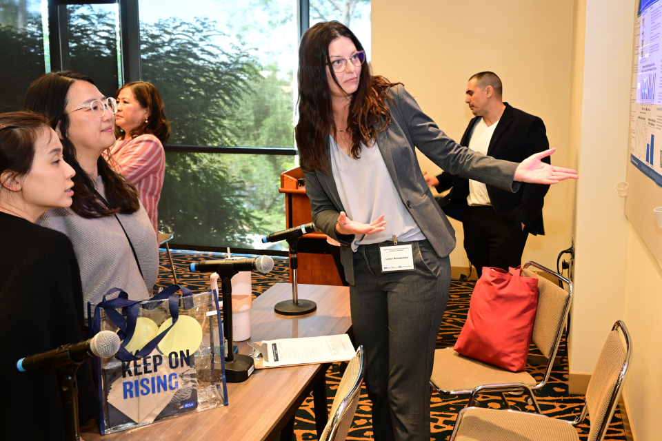 Woman presenting at conference pointing to screen as attendees watch.