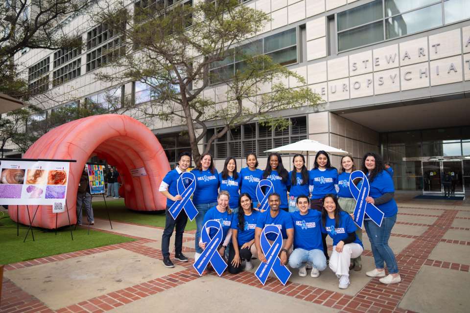 Group of people in blue shirts with awareness ribbons outside a building.