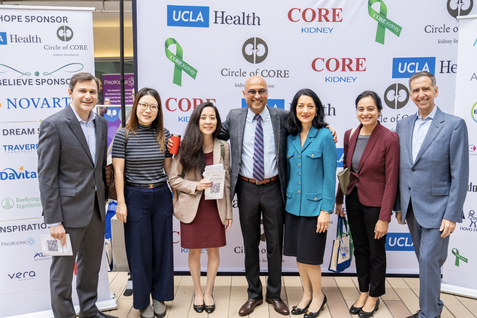 Seven people pose together at an event, smiling in front of sponsor banners.