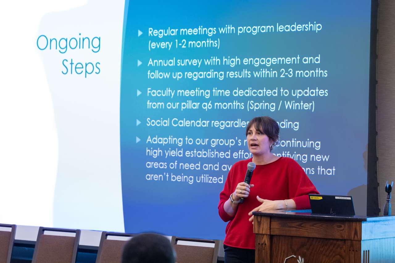 A woman presents at a conference on stage at a podium.