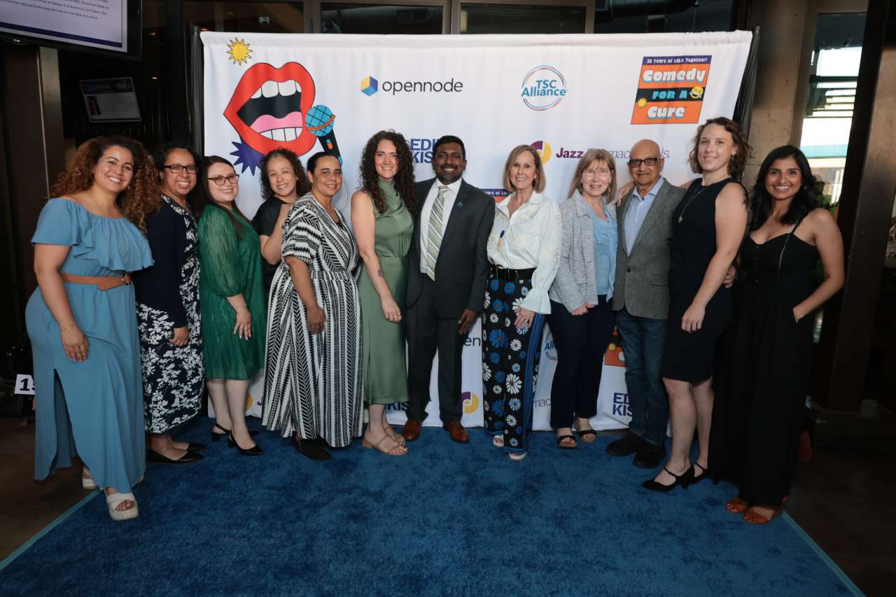 Dr. Raj Rajaraman (center) and colleagues from the UCLA Tuberous Sclerosis Complex Center of Excellence pose in front of a banner at the TSC Alliance Comedy for a Cure fundraiser in Irvine, CA.