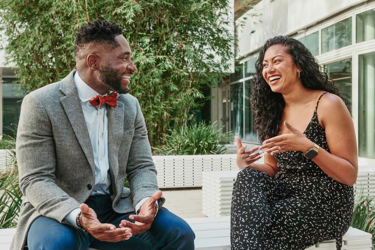Utibe R. Essien, MD, MPH and Jessica P. Faiz, MD siting on a concrete bench and chatting in an outdoor patio full of plants.