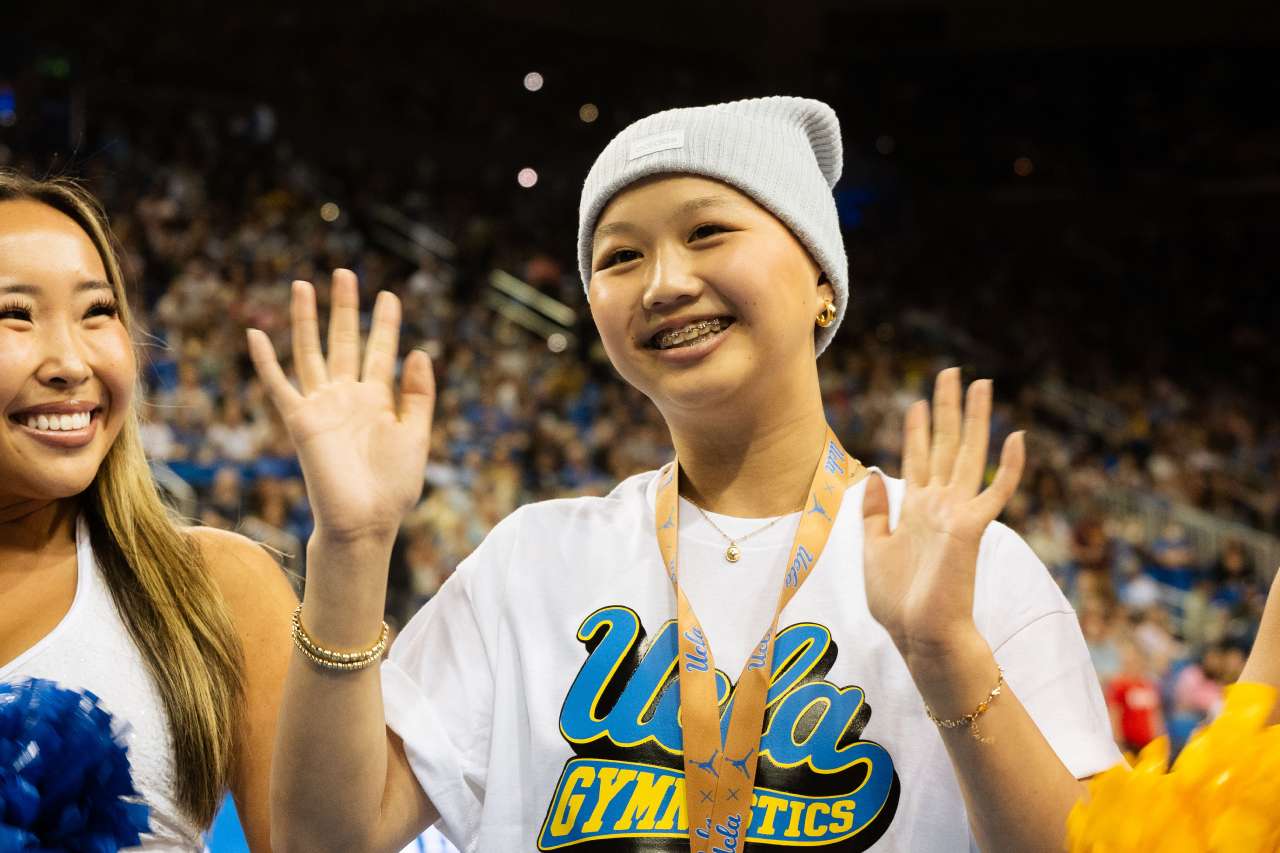A teen patient celebrates with two cheerleaders at a gymnastics meet.