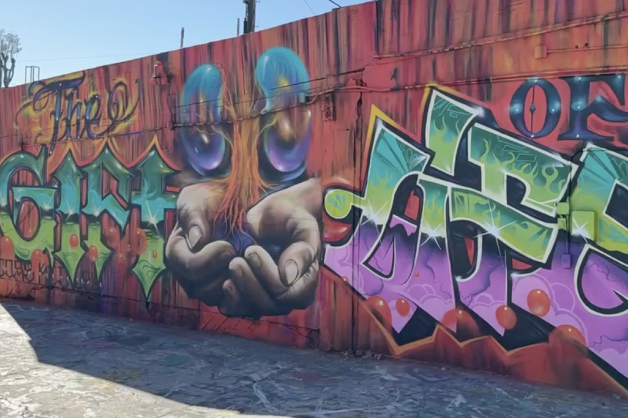 Colorful graffiti mural featuring hands and the text "Gift of Art."