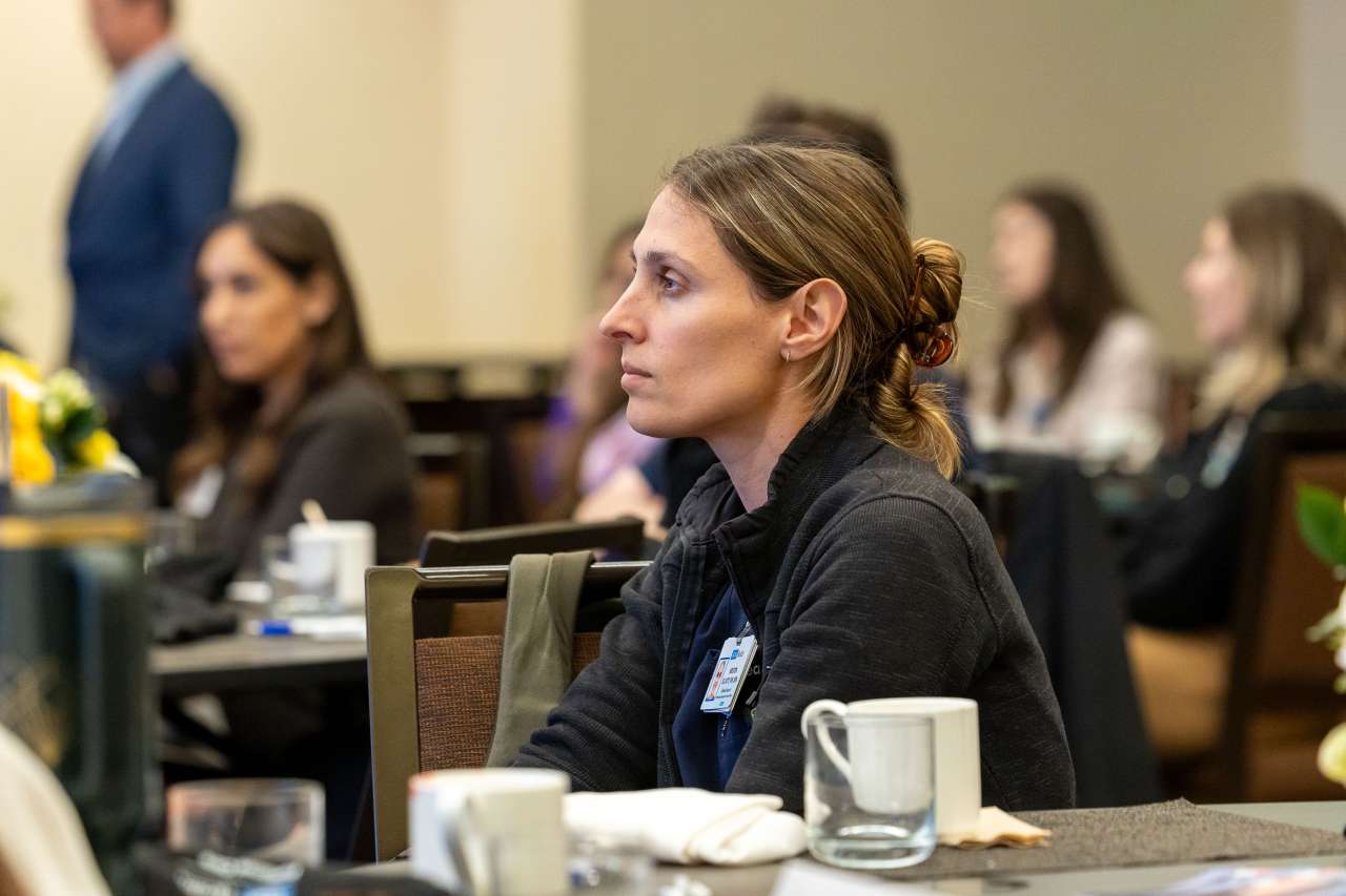 A woman watches a speaker presenting at a conference.