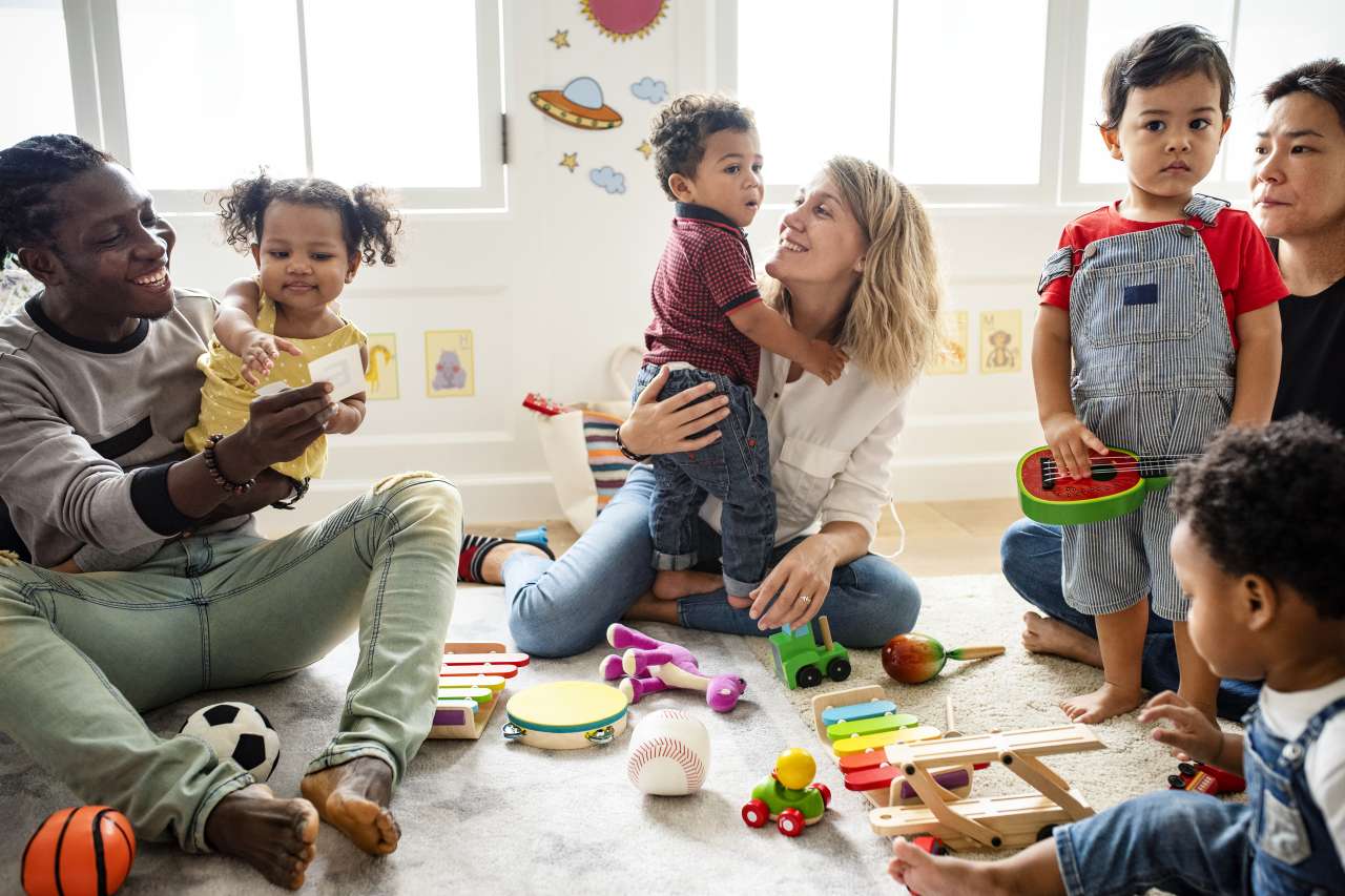 Daycare caregivers and toddlers sitting on floor playing with toys.