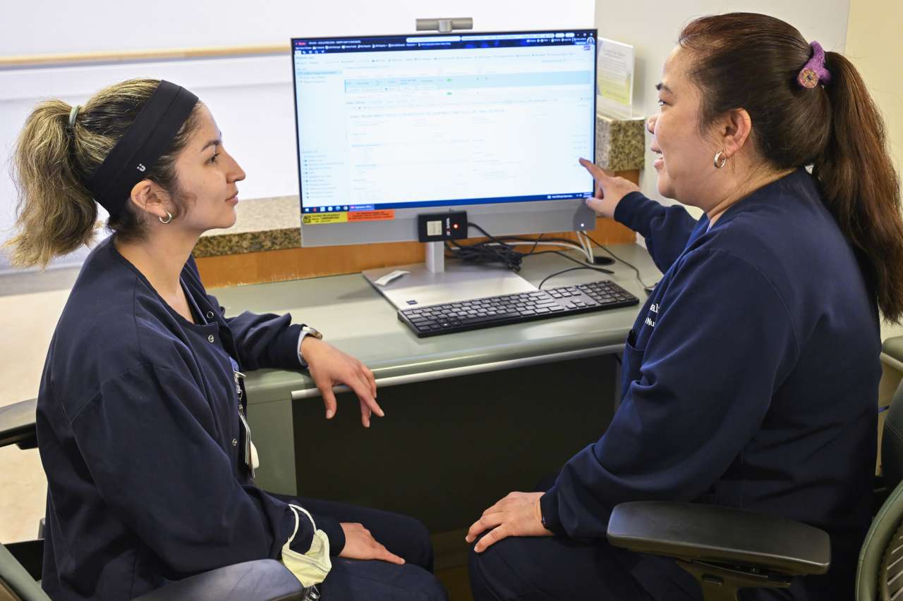 Two nurses sitting at a desk discussing results on a computer screen