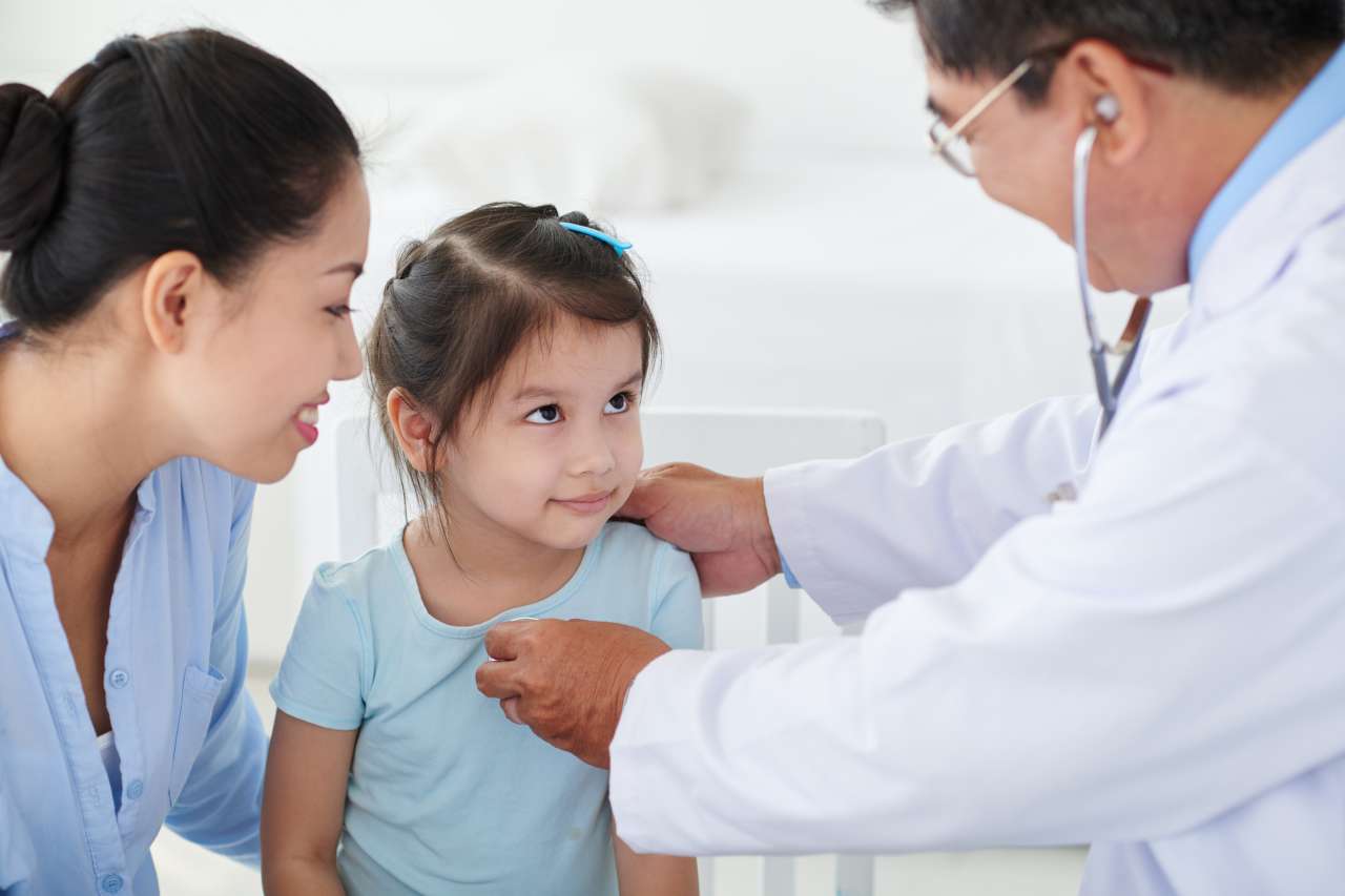 Doctor looking at his little patient while examining her with stethoscope.