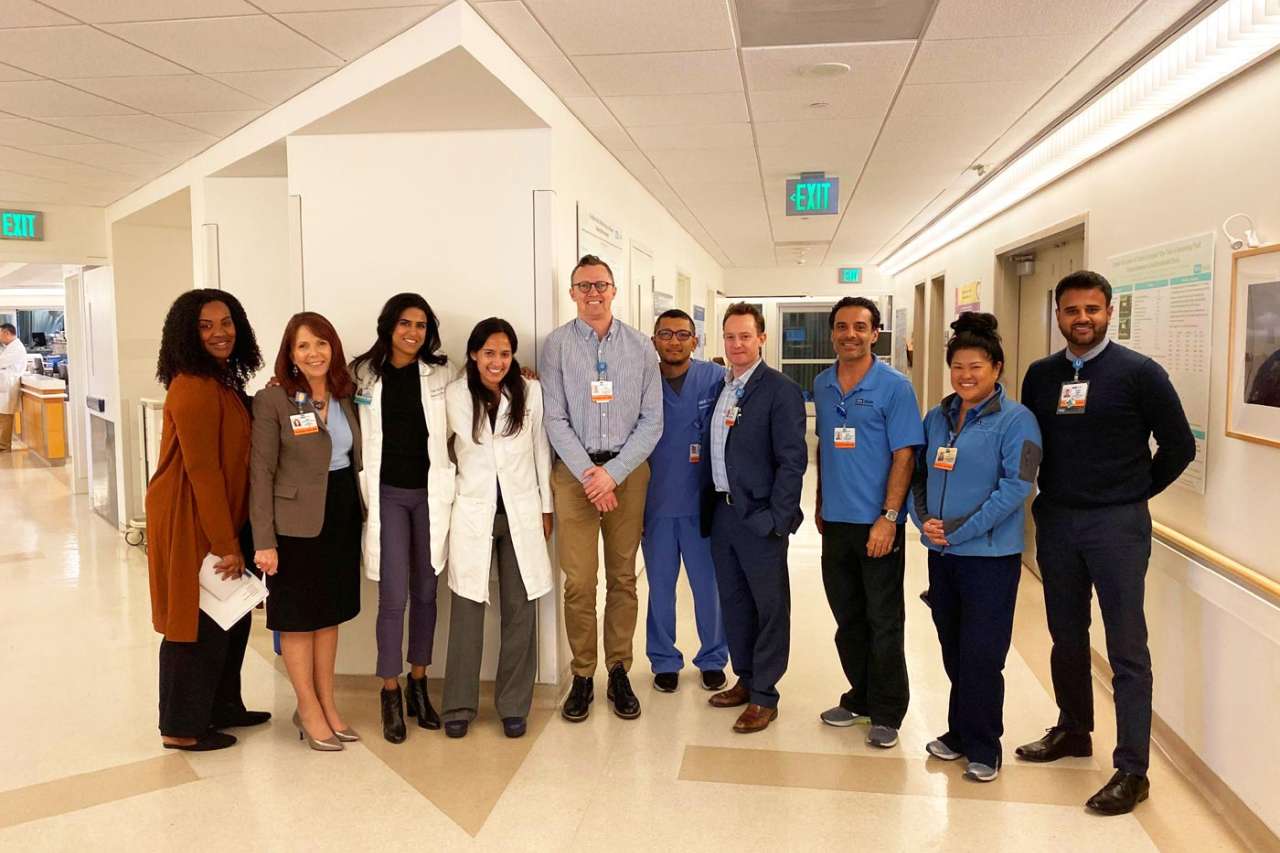 A group photo of the MICU team standing in a hospital hallway. They are wearing professional attire and some have hospital badges.
