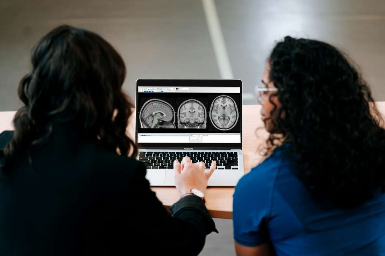 Two people look at a laptop screen showing three brain scans.