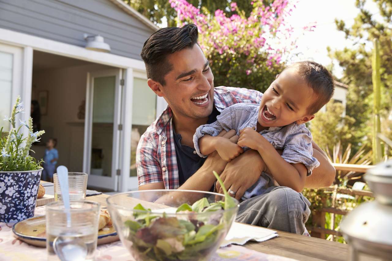 Father holding laughing young son at outdoor dining table