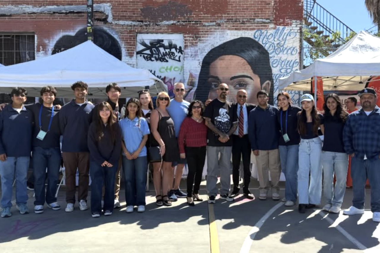Group photo of individuals standing in front of a mural with tents in the background.