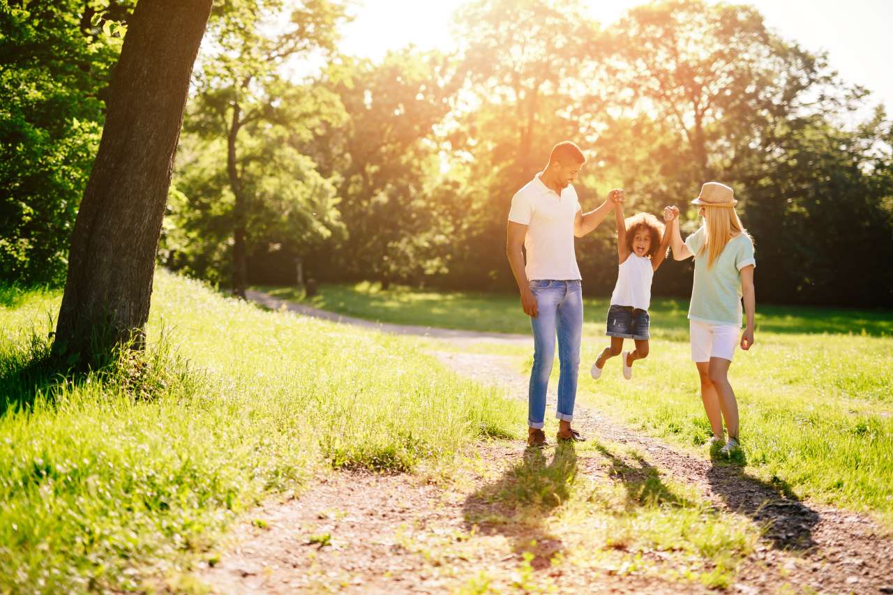 Two adults and two children on sunlit park path surrounded by trees