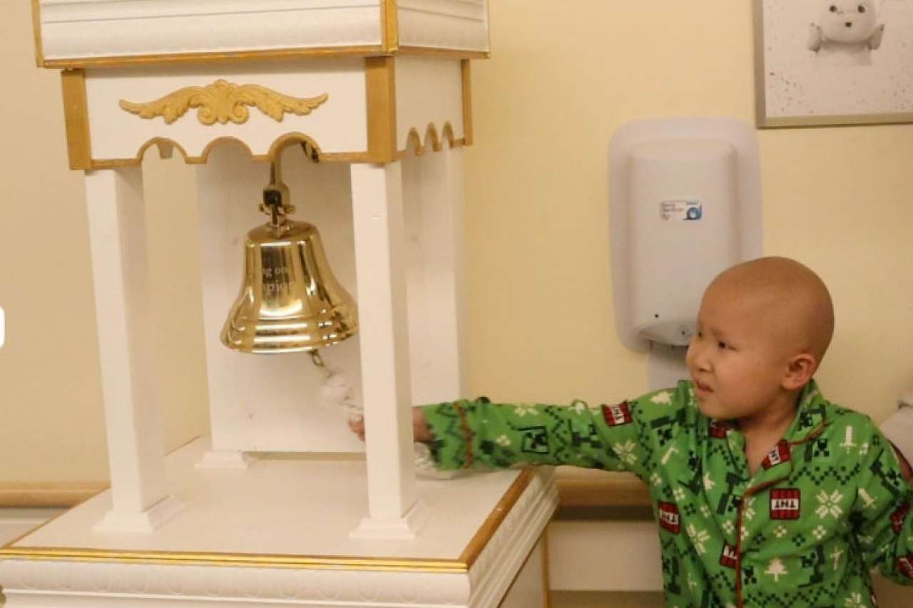 Child in pajamas reaching for a golden bell in a decorated play area.